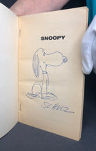 Load image into Gallery viewer, The front flyleaf featuring an original hand-drawn sketch of a smiling Snoopy in blue ballpoint pen, with the signature Schulz written directly below.
